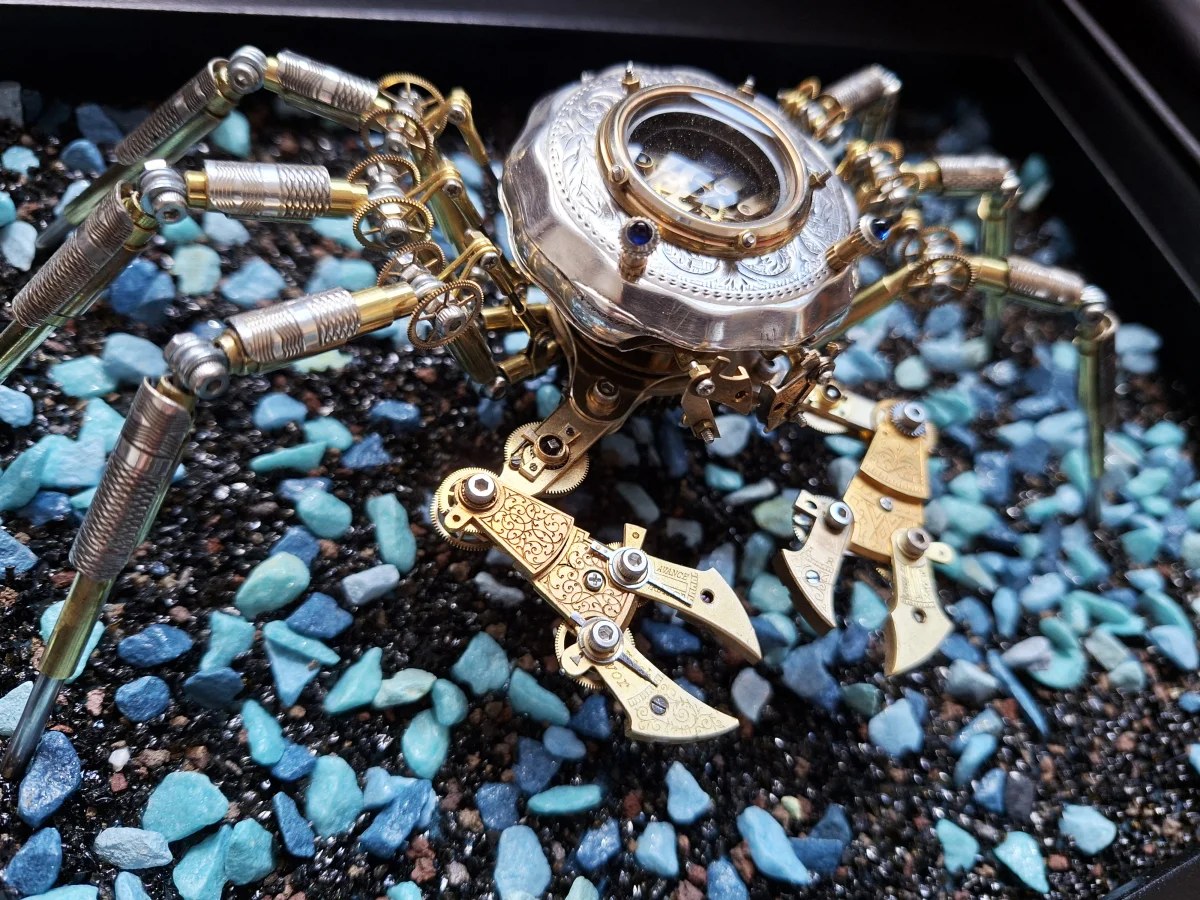 A steampunk crab sculpture with geared metal legs and brass plate claws on turquoise gravel